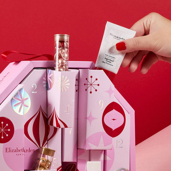 The pink Elizabeth Arden beauty advent calendar box with its skincare, makeup and fragrance products displayed peeking out of the boxes against a dark red backdrop.