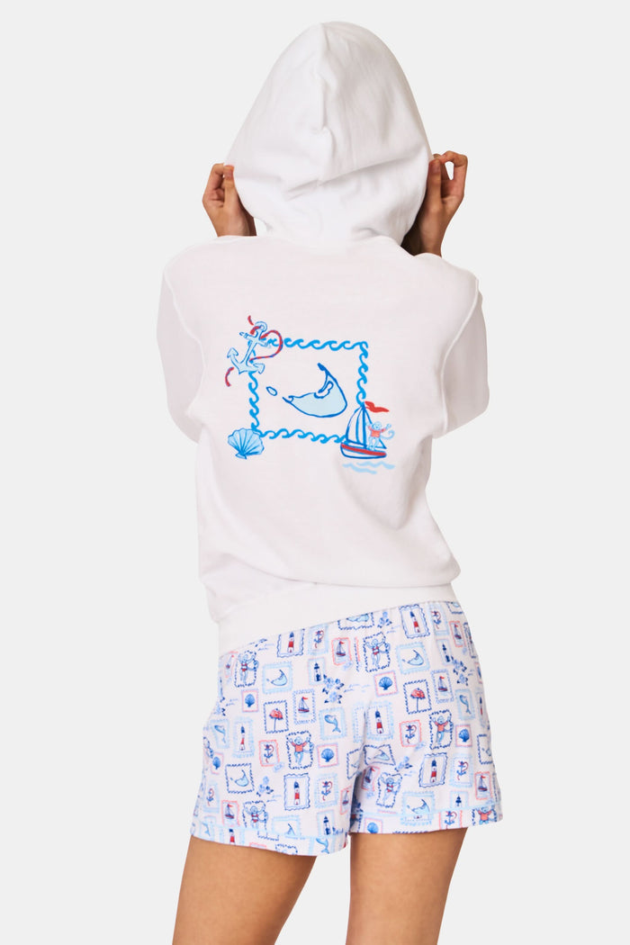A person wearing the Roller Rabbit ACK Zip Up hoodie, featuring a blue and red nautical design on the back, paired with patterned shorts and standing with their back to the camera and hood up.