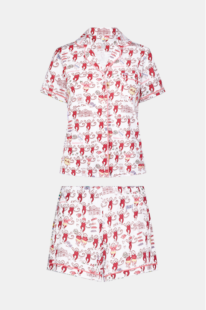 The Roller Rabbit Alpha Phi Monkey Polo Pajamas are a two-piece set crafted from soft Pima Cotton, featuring a white base adorned with playful red cartoon monkey prints and whimsical text. The short-sleeve top includes a front button placket, while the matching shorts feature an elastic waistband, all displayed on a plain background.