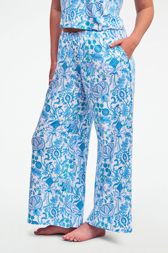 A woman stands barefoot on one leg, stretching with arms raised and eyes closed, wearing the Roller Rabbit Amanda Boden Pant and a matching blue floral short-sleeve pajama top.