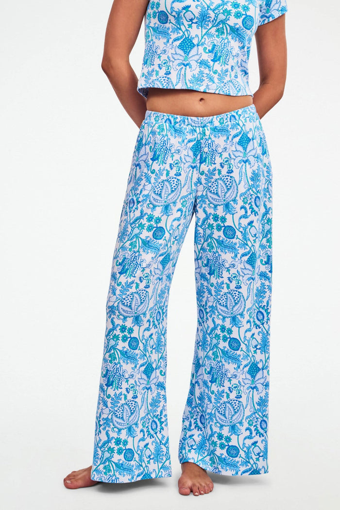A woman stands barefoot on one leg, stretching with arms raised and eyes closed, wearing the Roller Rabbit Amanda Boden Pant and a matching blue floral short-sleeve pajama top.