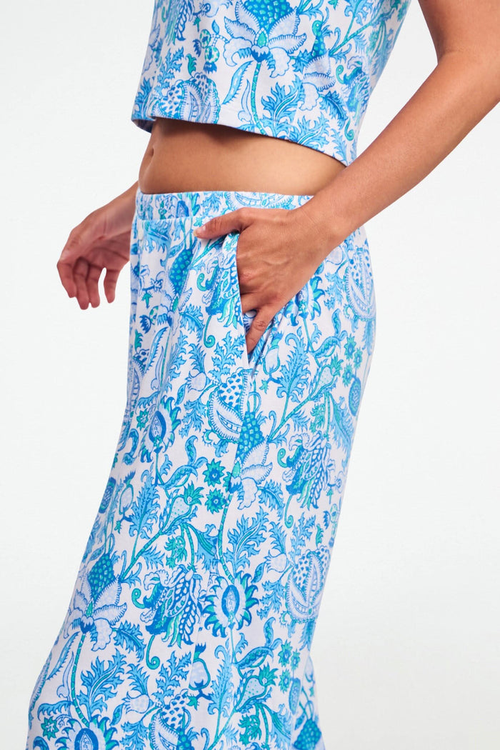 A woman stands barefoot on one leg, stretching with arms raised and eyes closed, wearing the Roller Rabbit Amanda Boden Pant and a matching blue floral short-sleeve pajama top.