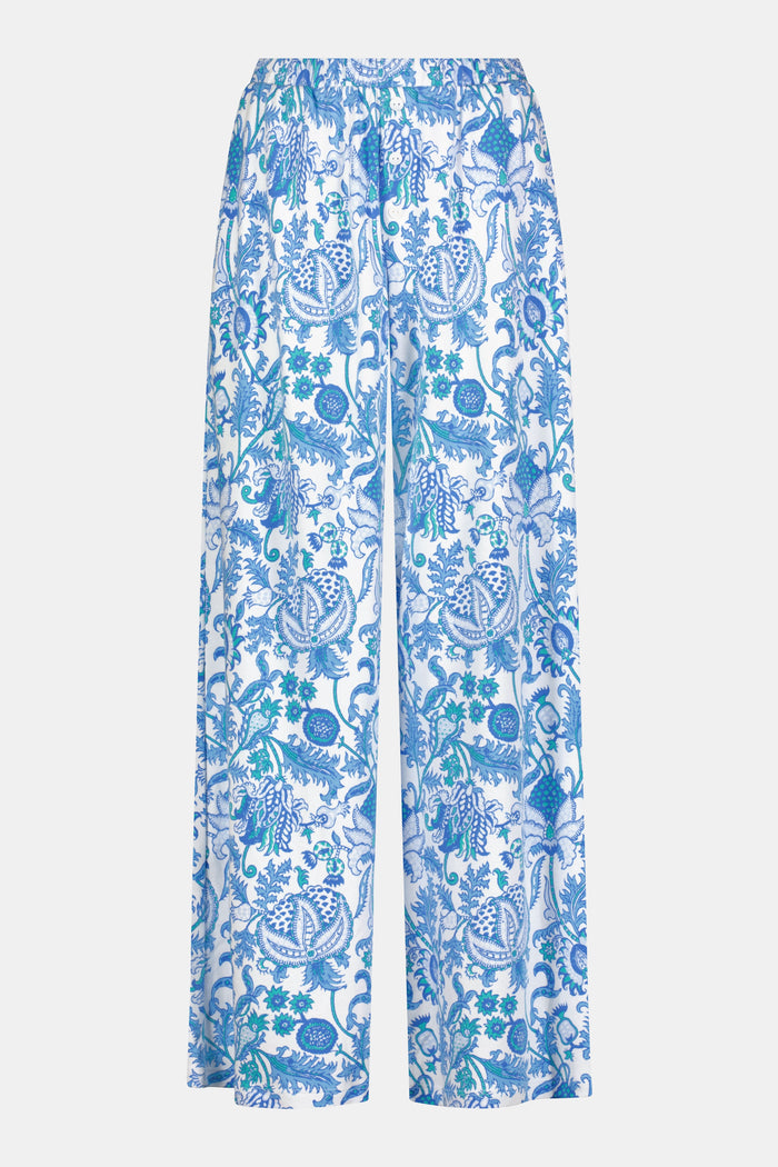 A woman stands barefoot on one leg, stretching with arms raised and eyes closed, wearing the Roller Rabbit Amanda Boden Pant and a matching blue floral short-sleeve pajama top.