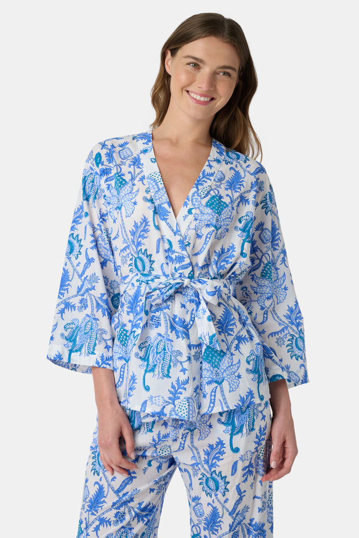 A woman poses barefoot against a plain white background wearing the Roller Rabbit Amanda Christy Set, a matching lounge set with a blue and white floral Amanda print, featuring a belted long-sleeve top and loose-fitting pants.