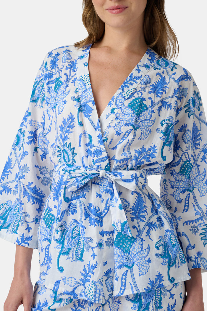A woman poses barefoot against a plain white background wearing the Roller Rabbit Amanda Christy Set, a matching lounge set with a blue and white floral Amanda print, featuring a belted long-sleeve top and loose-fitting pants.