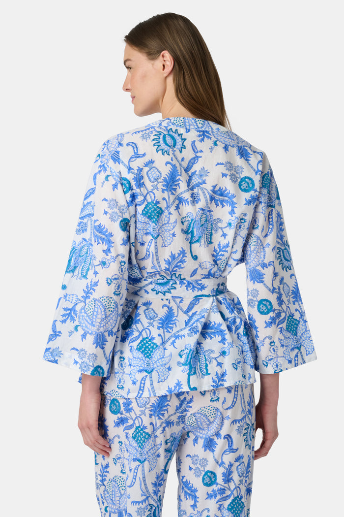 A woman poses barefoot against a plain white background wearing the Roller Rabbit Amanda Christy Set, a matching lounge set with a blue and white floral Amanda print, featuring a belted long-sleeve top and loose-fitting pants.