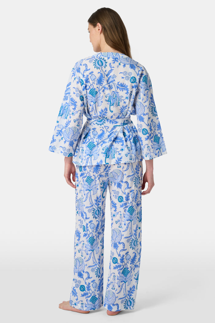 A woman poses barefoot against a plain white background wearing the Roller Rabbit Amanda Christy Set, a matching lounge set with a blue and white floral Amanda print, featuring a belted long-sleeve top and loose-fitting pants.
