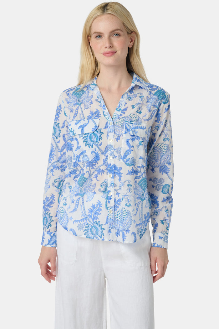 A woman with long blonde hair wears the Roller Rabbit Amanda Guy Shirt, a light blue and white paisley long-sleeve top, paired with white pants, standing against a plain white background.