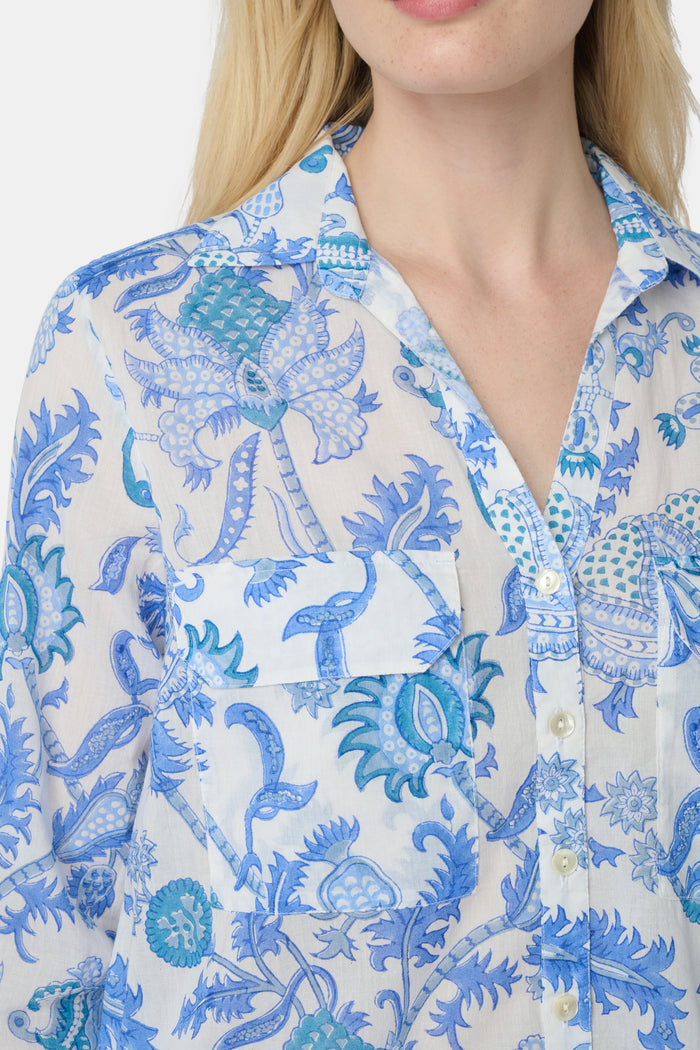 A woman with long blonde hair wears the Roller Rabbit Amanda Guy Shirt, a light blue and white paisley long-sleeve top, paired with white pants, standing against a plain white background.