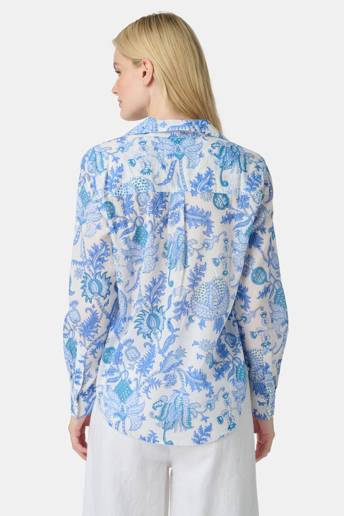 A woman with long blonde hair wears the Roller Rabbit Amanda Guy Shirt, a light blue and white paisley long-sleeve top, paired with white pants, standing against a plain white background.