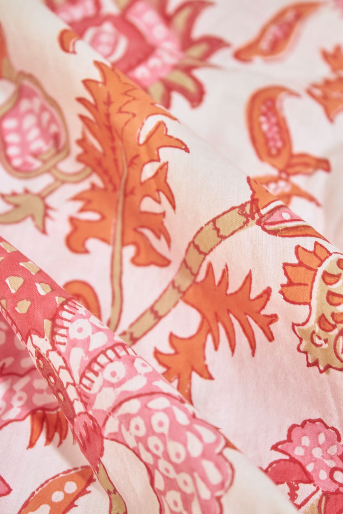 A woman with long blonde hair wears the Roller Rabbit Amanda Kimono, a belted, knee-length cotton kimono with a vibrant pink and orange floral pattern on white. She stands against a plain light gray backdrop, smiling softly.