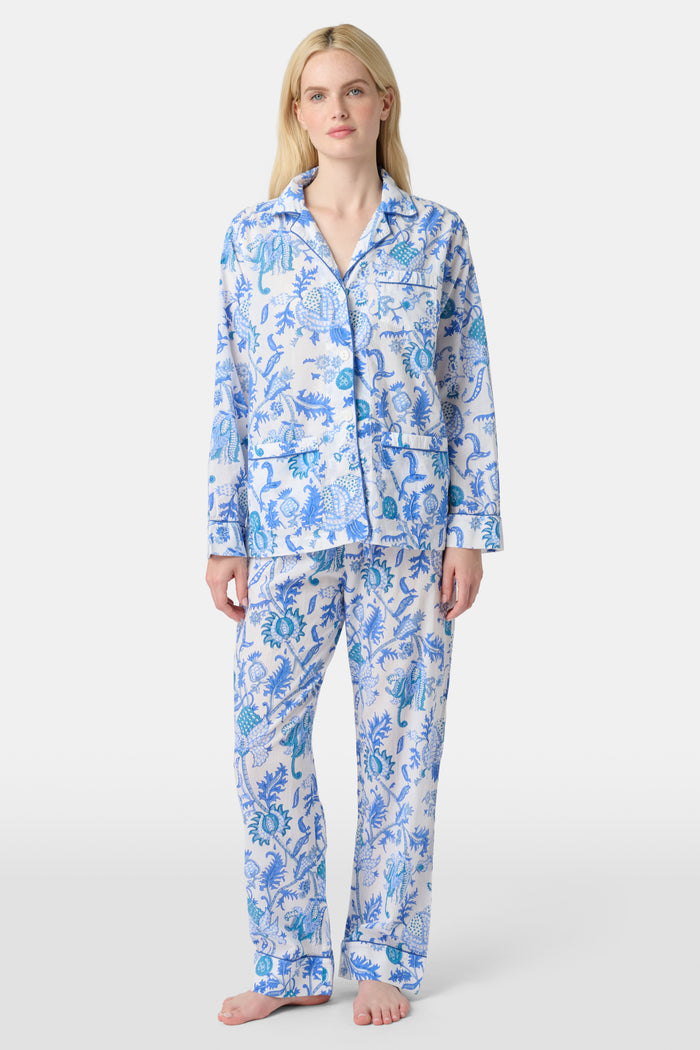 A woman stands barefoot in the Amanda Loungewear set by Roller Rabbit, featuring a blue and white botanical print, long-sleeve collared button-up shirt, and matching pants against a plain light background.