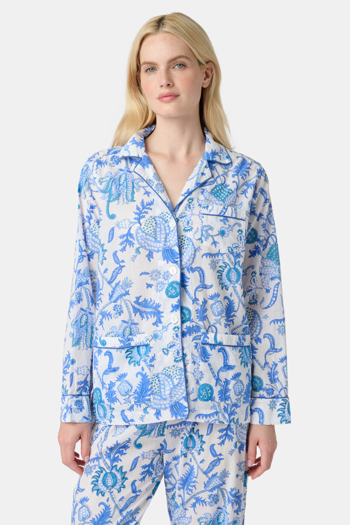A woman stands barefoot in the Amanda Loungewear set by Roller Rabbit, featuring a blue and white botanical print, long-sleeve collared button-up shirt, and matching pants against a plain light background.