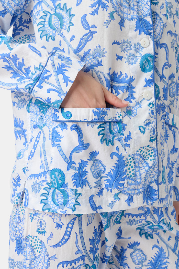 A woman stands barefoot in the Amanda Loungewear set by Roller Rabbit, featuring a blue and white botanical print, long-sleeve collared button-up shirt, and matching pants against a plain light background.
