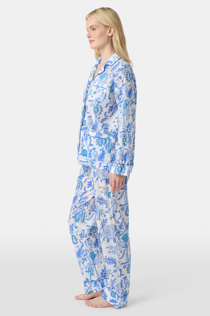 A woman stands barefoot in the Amanda Loungewear set by Roller Rabbit, featuring a blue and white botanical print, long-sleeve collared button-up shirt, and matching pants against a plain light background.