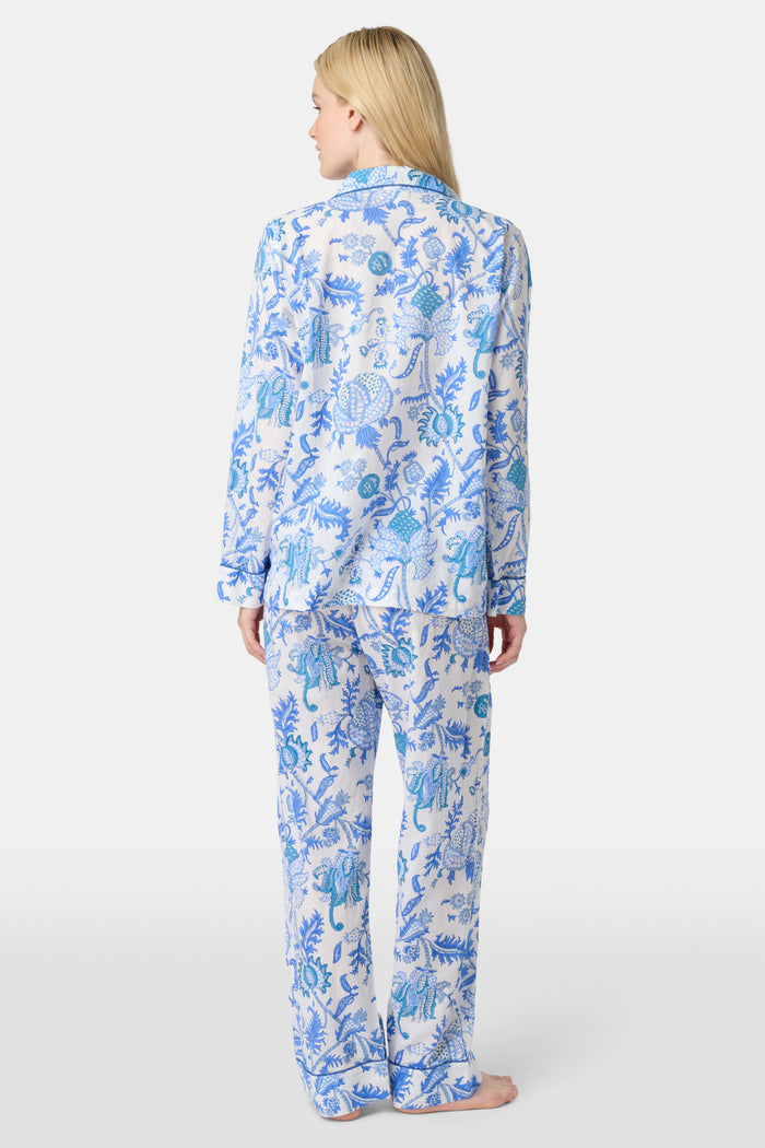 A woman stands barefoot in the Amanda Loungewear set by Roller Rabbit, featuring a blue and white botanical print, long-sleeve collared button-up shirt, and matching pants against a plain light background.