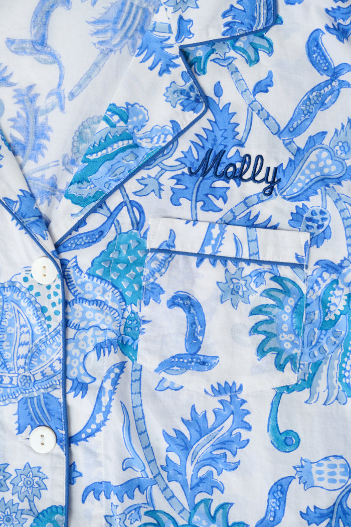 A woman stands barefoot in the Amanda Loungewear set by Roller Rabbit, featuring a blue and white botanical print, long-sleeve collared button-up shirt, and matching pants against a plain light background.