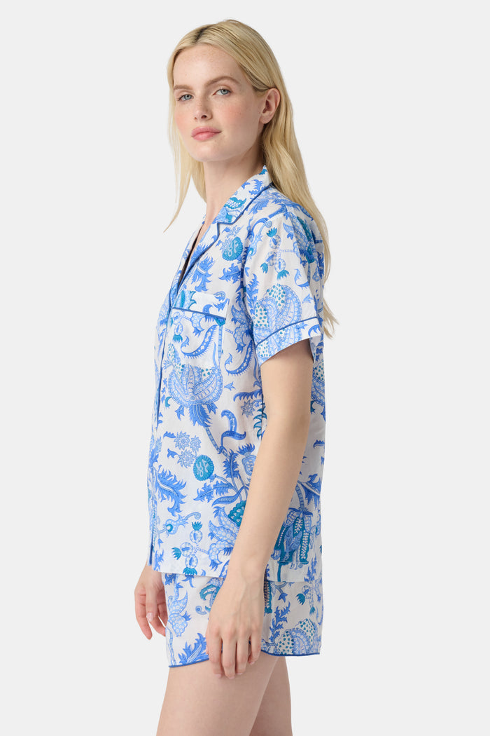 A woman with long blonde hair smiles in the Amanda Lulu Set by Roller Rabbit, a blue floral print cotton short set, standing against a plain light background and showcasing this chic women's loungewear.