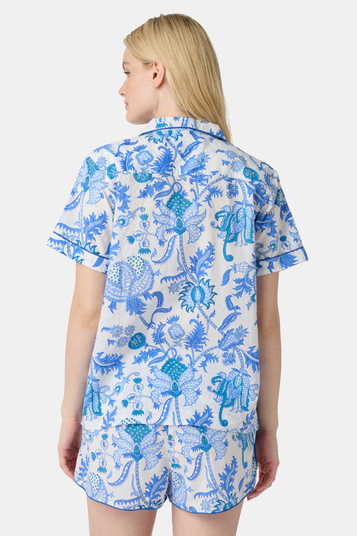 A woman with long blonde hair smiles in the Amanda Lulu Set by Roller Rabbit, a blue floral print cotton short set, standing against a plain light background and showcasing this chic women's loungewear.