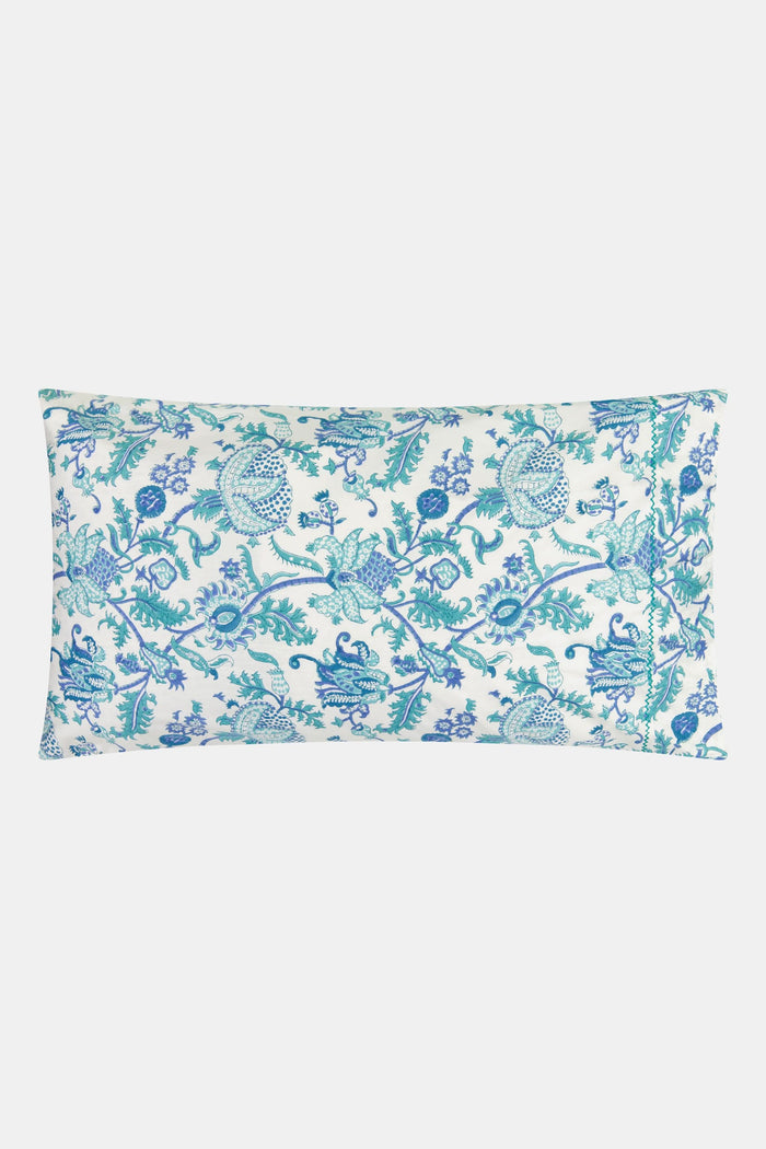 Two pillows with Amanda Pillowcase Set by Roller Rabbit rest on blue and turquoise floral bedding; the 100 cotton pillowcases coordinate with a white, leafy headboard and white curtains in the background.