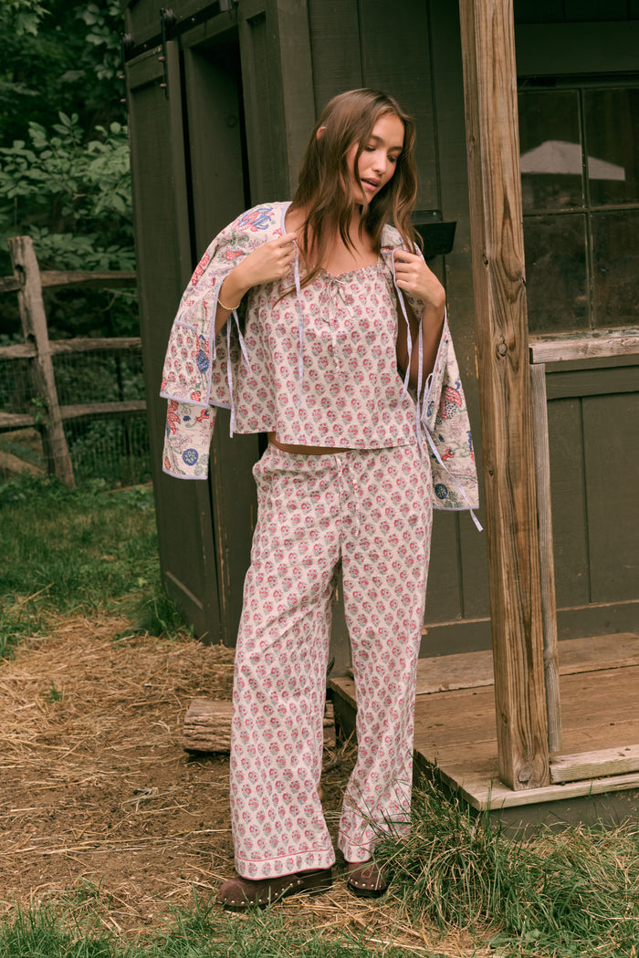 A woman stands facing forward against a plain white background, wearing the Roller Rabbit Amanda Sophie Jacket—a reversible cotton piece featuring blue, red, and pink floral and abstract designs—paired with cream-colored pants.