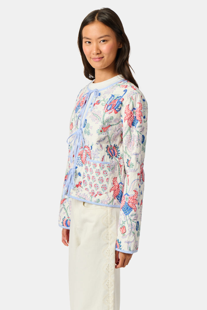 A woman stands facing forward against a plain white background, wearing the Roller Rabbit Amanda Sophie Jacket—a reversible cotton piece featuring blue, red, and pink floral and abstract designs—paired with cream-colored pants.