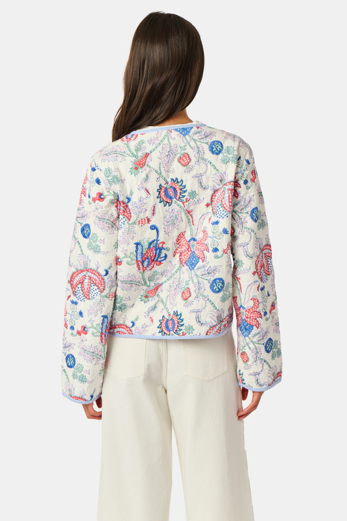 A woman stands facing forward against a plain white background, wearing the Roller Rabbit Amanda Sophie Jacket—a reversible cotton piece featuring blue, red, and pink floral and abstract designs—paired with cream-colored pants.