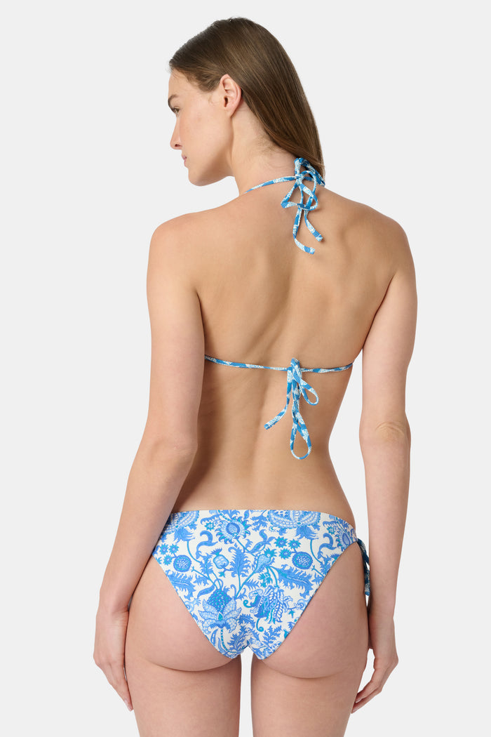 A person wears the Roller Rabbit Amanda/Jemina Serena Bikini Bottom, a reversible bikini with blue floral patterns, side ties, and UPF 50+ sun protection, standing against a plain white background.