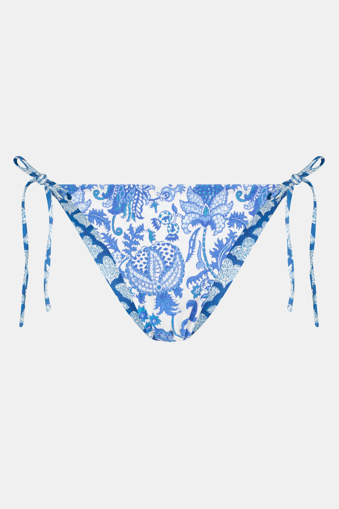 A person wears the Roller Rabbit Amanda/Jemina Serena Bikini Bottom, a reversible bikini with blue floral patterns, side ties, and UPF 50+ sun protection, standing against a plain white background.