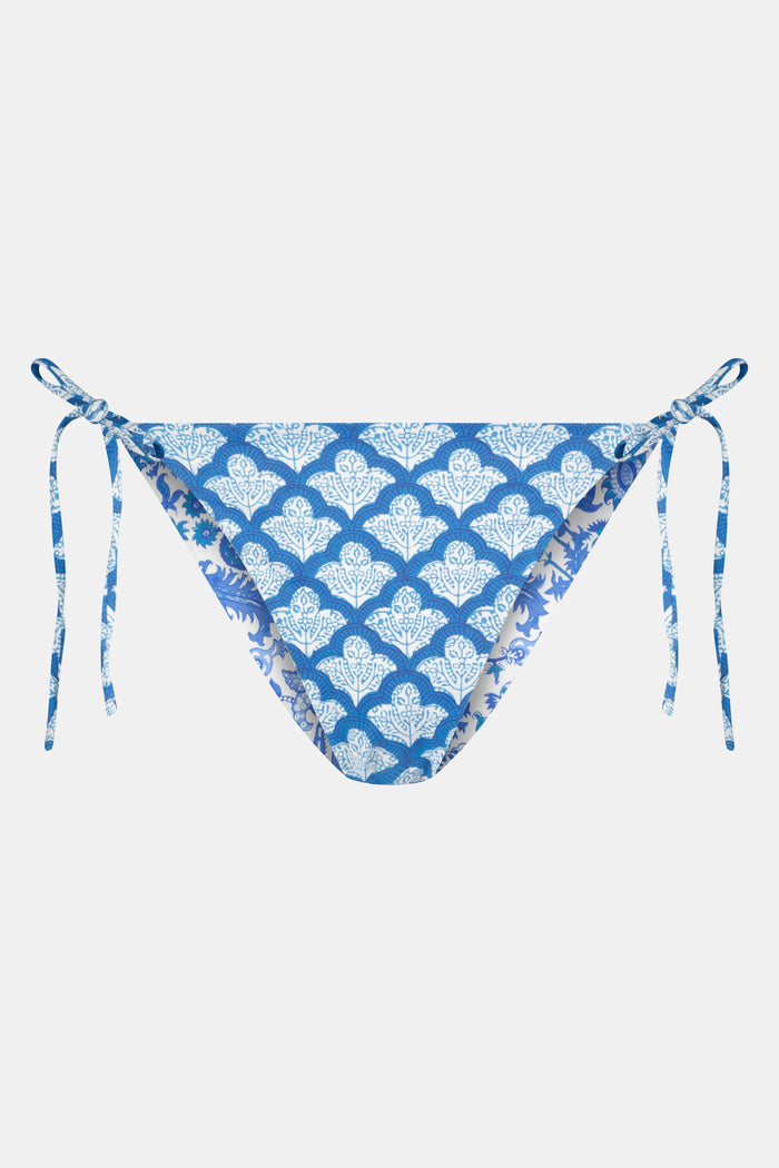 A person wears the Roller Rabbit Amanda/Jemina Serena Bikini Bottom, a reversible bikini with blue floral patterns, side ties, and UPF 50+ sun protection, standing against a plain white background.