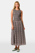 A woman wearing the Roller Rabbit Amelia Emma Dress, featuring a smocked bodice and maxi skirt, stands against a plain white background, paired with green polka-dot flats.