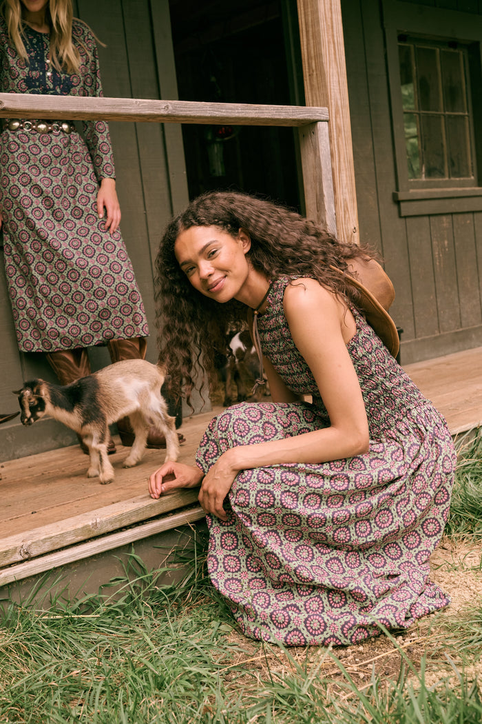 A woman wearing the Roller Rabbit Amelia Emma Dress, featuring a smocked bodice and maxi skirt, stands against a plain white background, paired with green polka-dot flats.