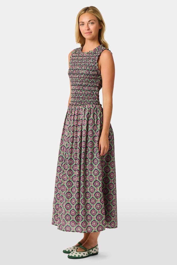 A woman wearing the Roller Rabbit Amelia Emma Dress, featuring a smocked bodice and maxi skirt, stands against a plain white background, paired with green polka-dot flats.