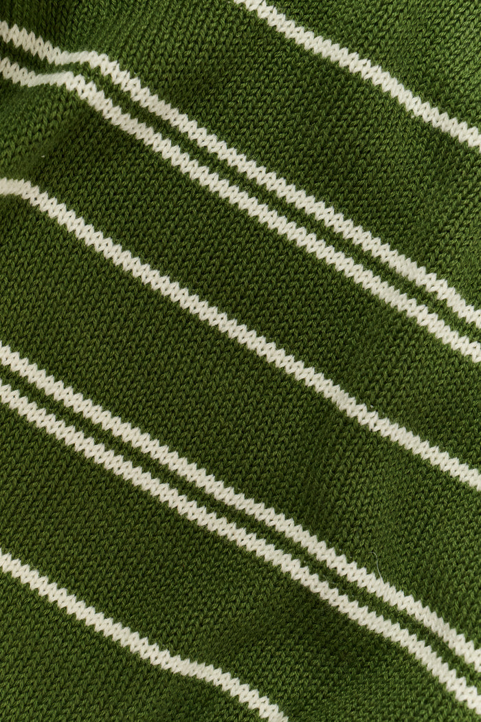 A person wearing the Roller Rabbit Autumn Stripe Olivia Pant—green and white striped, pull-on, flared—and a matching sweater lifts the hem to reveal their midriff. Brown slippers are visible. The background is white.