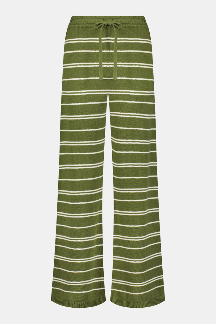 A person wearing the Roller Rabbit Autumn Stripe Olivia Pant—green and white striped, pull-on, flared—and a matching sweater lifts the hem to reveal their midriff. Brown slippers are visible. The background is white.