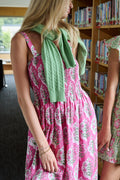 The Kids Ava Floral Ceri Dress by Roller Rabbit is a sleeveless baby dress featuring a smocked bodice and ruffled straps, adorned with green and white leaf patterns on a vibrant pink background, and comes with matching bloomers.