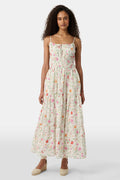 A woman with curly hair wears the Roller Rabbit Baroque Floral Karla Dress, a sleeveless ankle-length sundress with a smocked bodice, paired with beige espadrille flats against a plain light background.