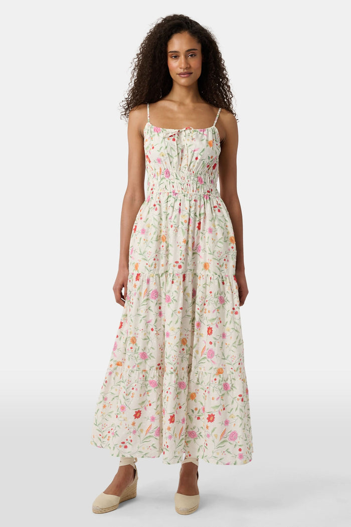 A woman with curly hair wears the Roller Rabbit Baroque Floral Karla Dress, a sleeveless ankle-length sundress with a smocked bodice, paired with beige espadrille flats against a plain light background.
