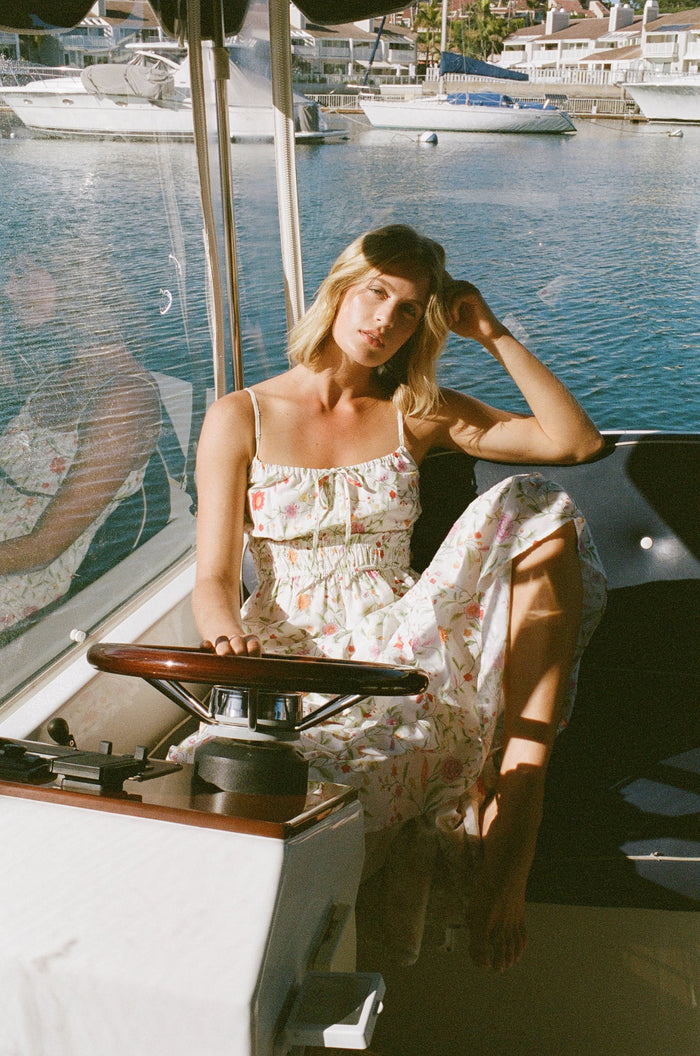 A woman with curly hair wears the Roller Rabbit Baroque Floral Karla Dress, a sleeveless ankle-length sundress with a smocked bodice, paired with beige espadrille flats against a plain light background.