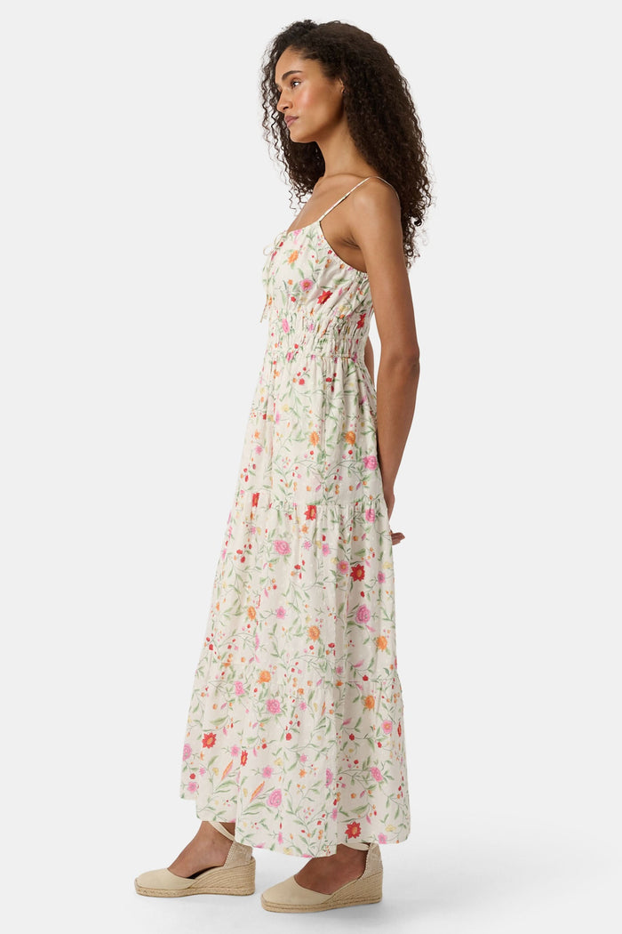 A woman with curly hair wears the Roller Rabbit Baroque Floral Karla Dress, a sleeveless ankle-length sundress with a smocked bodice, paired with beige espadrille flats against a plain light background.