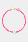 The Beaded Charm Necklace by Roller Rabbit features round pink beads and a small gold ring centerpiece, completed with a gold adjustable clasp and chain. This semi-precious stone necklace is shown against a plain white background.