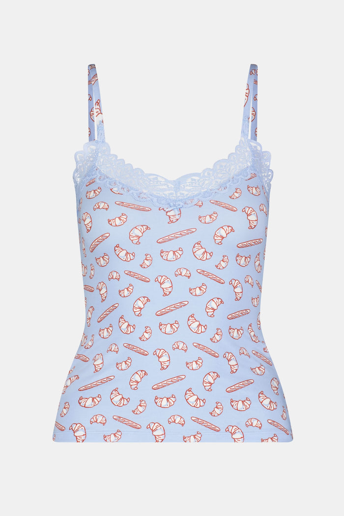 A woman models the Roller Rabbit Breakfast In Bread Perry Cami, featuring scalloped lace trim and a playful croissant print. The photo is cropped from shoulders to hips against a plain white background.