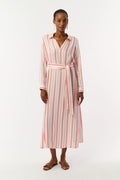 A woman with short hair and gold earrings wears the Roller Rabbit Cabana Stripe Fallon Dress—an ankle-length, long-sleeve vacation dress with vertical red stripes and a matching waist tie—paired with brown sandals against a white background.