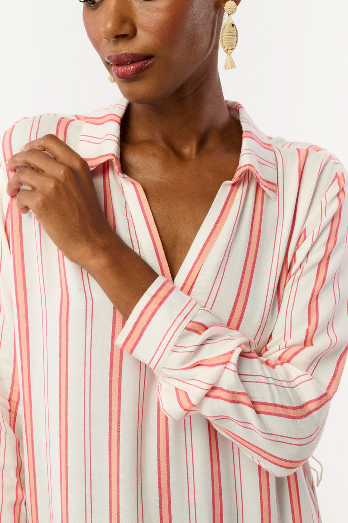 A woman with short hair and gold earrings wears the Roller Rabbit Cabana Stripe Fallon Dress—an ankle-length, long-sleeve vacation dress with vertical red stripes and a matching waist tie—paired with brown sandals against a white background.