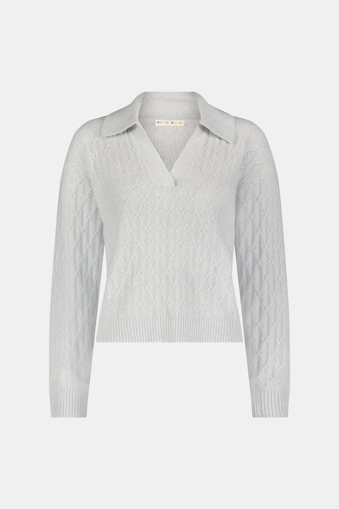 A woman wearing a light gray Cable Knots Rocio Sweater by Roller Rabbit, featuring a textured knit and V-neck, paired with matching knit pants, stands against a plain white background.