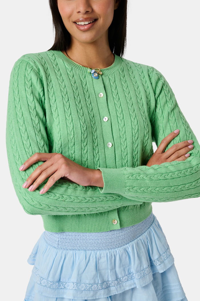 The Roller Rabbit Cable Stripe Moxie Cardigan is a bright forest green, long-sleeve cardigan featuring a cable-knit design. Crafted from soft cotton cashmere, it has a crew neckline and gold buttons down the front, shown against a plain white background.