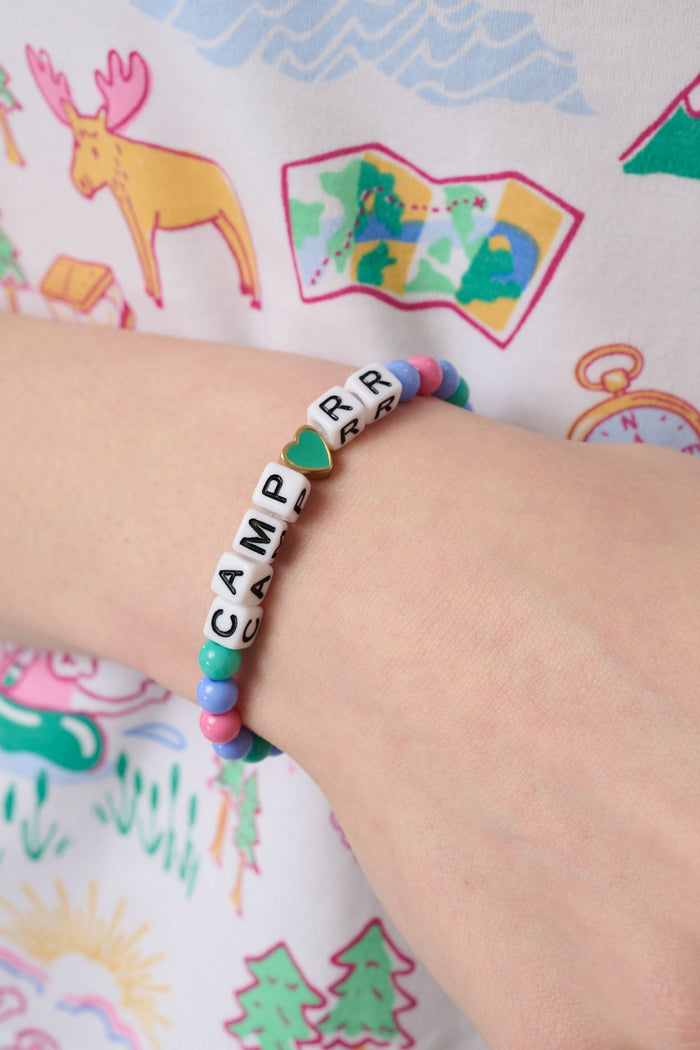 The Roller Rabbit Camp RR Besties Bracelet features pink, blue, and green beads, a blue star bead, white letter beads spelling CAMP R R with a gold-edged green heart as the "O"—a perfect colorful accessory for summer.