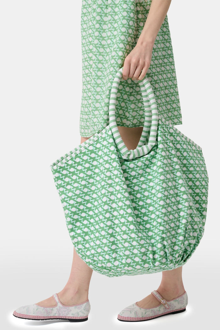 The Cane Bondi Bag by Roller Rabbit is a green and white tote with a wide, round handle, side ties, and a repeating fish pattern on soft cotton canvas. Its unique flared shape adds style to this charming everyday bag.