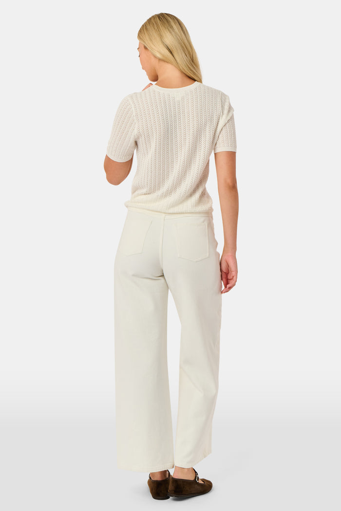 A woman wearing the Roller Rabbit Chain Pointelle Lauren Sweater in cream and white pants, standing against a white background.
