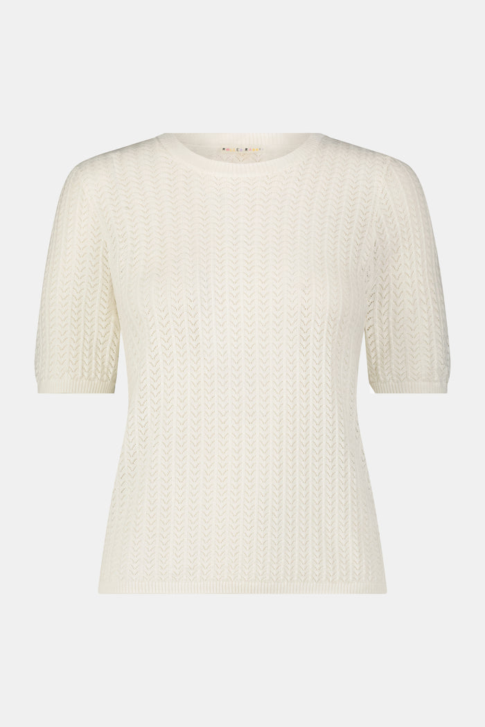 A woman wearing the Roller Rabbit Chain Pointelle Lauren Sweater in cream and white pants, standing against a white background.